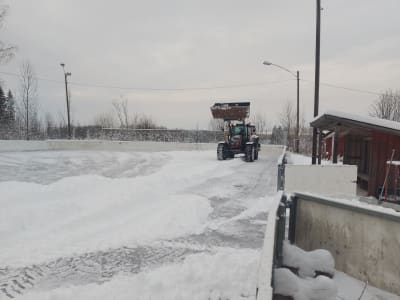 En traktor plogar snö bort från isen på Isnäs sportplan.