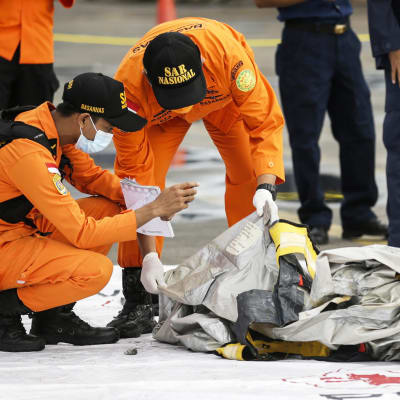 Pelastustyöntekijät tutkivat merestä löytyneitä lentokoneen osia.