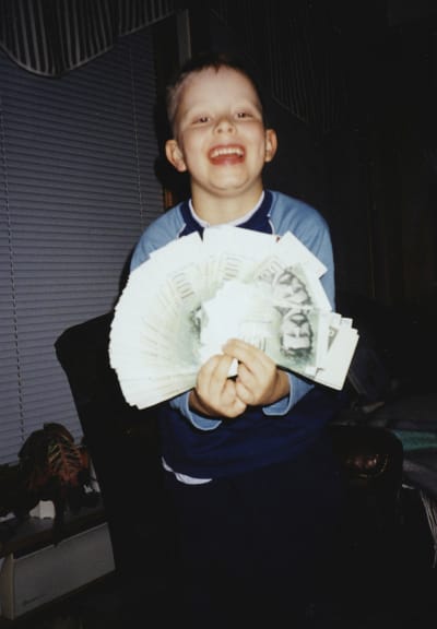 Hymyilevä poika levittää 100 markan seteleitä viuhkaksi