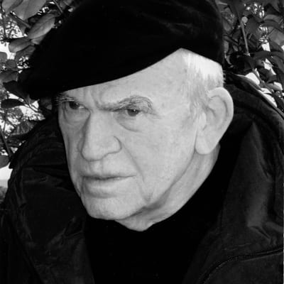 Svartvitt foto på Milan Kundera. Kundera har ett neutralt men koncentrerat ansiktsuttryck.