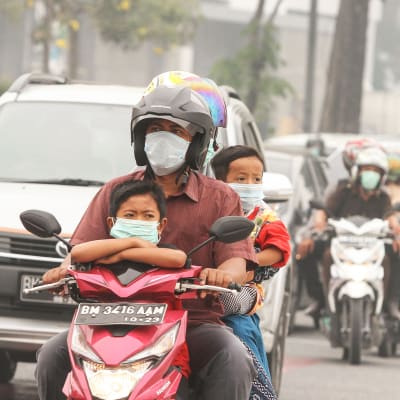 Hengityssuojaimilla varustautunut perhe ajamassa skootterilla Pekanbarussa, Indonesiassa.