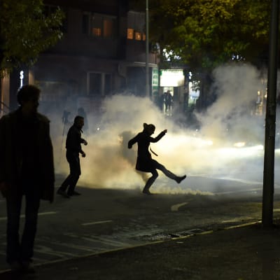 Opposition kannattaja potkaisi poliisin heittämämää kyynelkaasupulloa Pristinassa 12. lokakuuta.