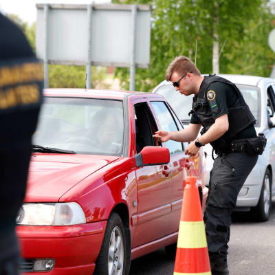 En gränsövervakare talar med en person som sitter i en röd bil.