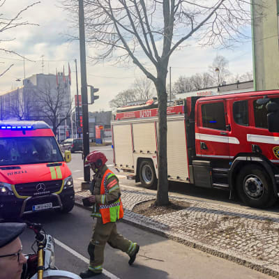En ambulans och en brandbil på en gata. Räddningspersonal går mellan bilarna och nyfikna förbipasserare står intill.