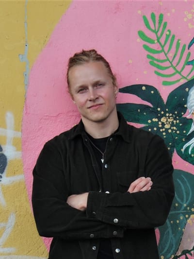 Helsingfors Universitets avhandlingsforskare Riku Löf står framför en färggrann vägg.