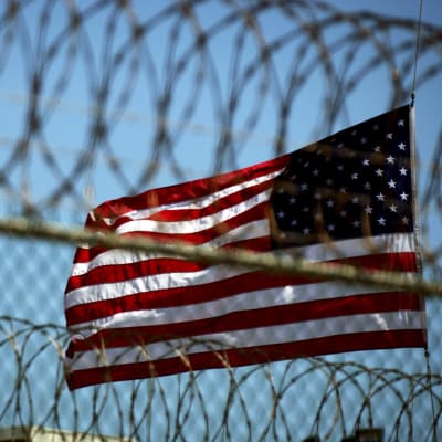 En amerikansk flagga bakom taggtråd som omger fånglägret Guantanamo Bay
