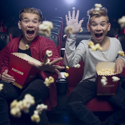 Marcus ja Martinus istuvat elokuvateatterissa, nauravat ja heittävät popcornia kohti kameraa.