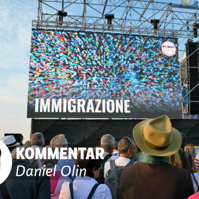 Människor framför scen med bild där det står immigrazione. I förgrunden texten kommentar Daniel Olin och en liten bild på en man.