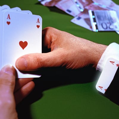 En hand håller i spelkort, på bordet ligger sedlar.