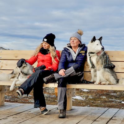 Krista och Lotta och två hundar sitter på en bänk och njuter av naturen.