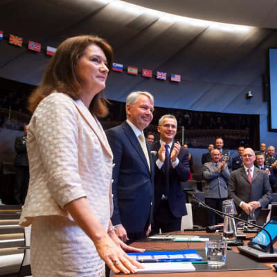 Ann Linde, Pekka Haavisto ja Jens Stoltenberg seisovat allekirjoitusseremoniassa kokoushuoneessa.