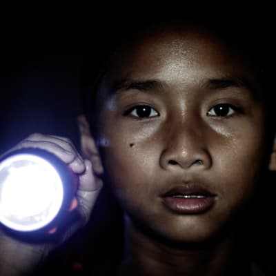 Närbild på en liten pojke som lyser med en flicklampa.