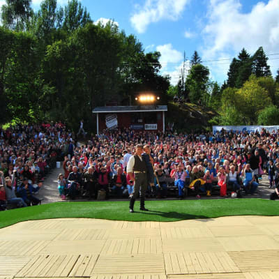 En person står på en scen med en stor publik bakom sig.