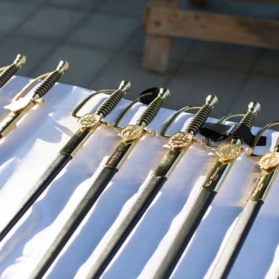 Auringossa kiiltäviä miekkoja rivissä valkoisen pöytäliinan päällä.