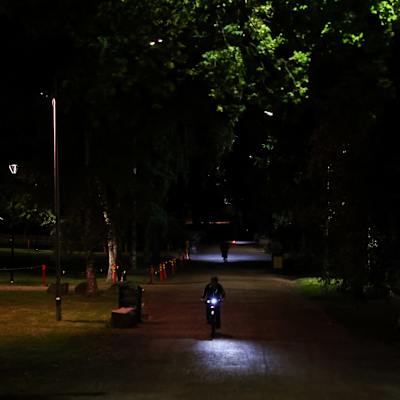 Pimeä Kaisaniemen puisto, jonka etualla pyöräilee ihminen. Kuva on otettu alkuyöstä.