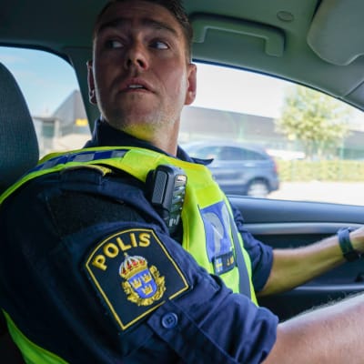 Polisinspektör Jonas Berg tittar över axeln då han kör bil.
