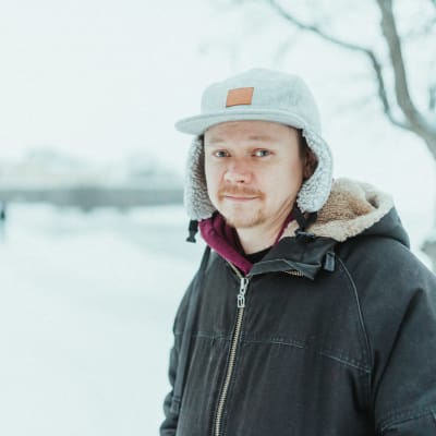 Rap-artisti Talonpoika Lalli katsoo hymyillen kameraan talvisessa maisemassa seisten.
