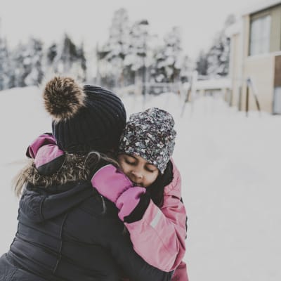ett barn kramar om en vuxen ute på en snöig gård.