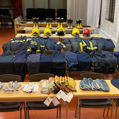 Erilaisia pelastushenkilöstön tarvikkeita ja vaatteita aseteltuna riveihin pöydälle.