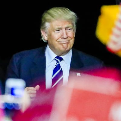 Trump hymyilee kuvan keskellä sinisessä puvussaan ja sinivalkoisessa solmiossa.