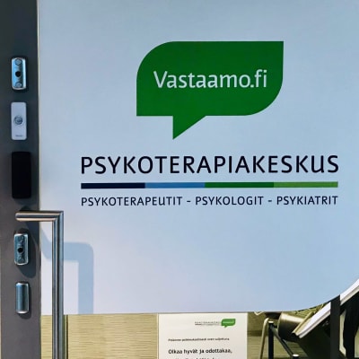 Glasvägg och glasdörr in i ett väntrum. På dörren finns texten Vastaamo Psykoterapiakeskus.