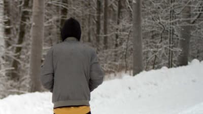 30-åriga Ali på en snöig skogsväg i Finland. Han står med ryggen vänd mot kameran och en huva på huvudet.