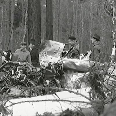 Miehiä mustavalkoisessa kuvassa metsään pudonneen lentokoneen hylyn luona.