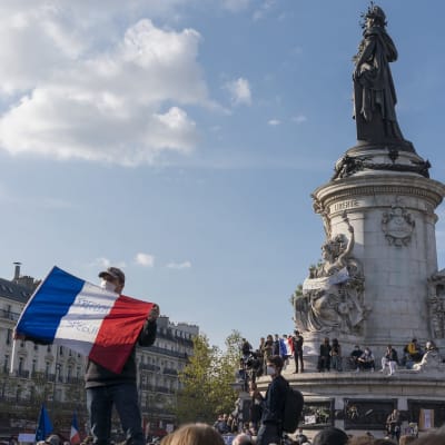 Mies pitelee Ranskan lippua aukiolle, jossa on myös paljon muita ihmisiä.