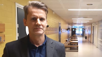 Man med blå skjorta och grå kavaj står i en tom skolkorridor.