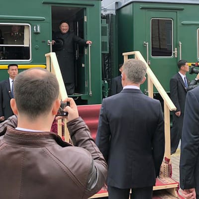 Kim Jong-un seisoo junan oviaukossa. Laiturilla on useita ihmisiä.
