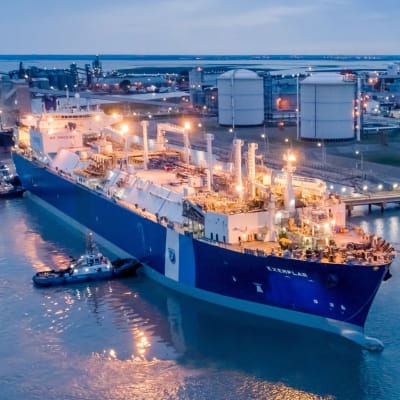 Ett stort fartyg vid en hamn intill fasinfrastruktur. På det blåa fartyget står det "Exemplar".