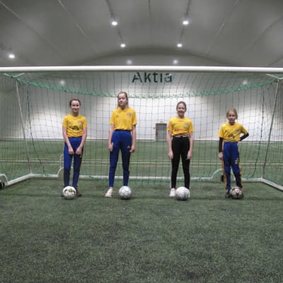 Fyra flickor står på rad vid ett fotbollsmål.