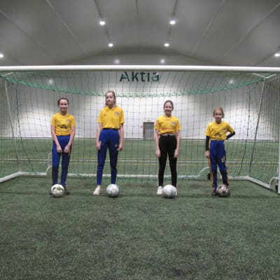 Fyra flickor står på rad vid ett fotbollsmål.