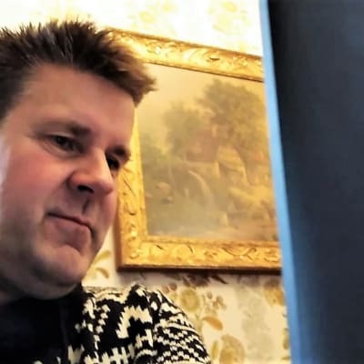 En medelåldersmans ansikte, han tittar på en datorskärm. I bakgrunden syns en tavla på väggen.