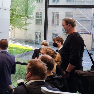 Den åtalade står utanför rättssalen omringad av media.