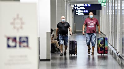 Två resenärer går med varsin kappsäck på Helsingfors-Vanda flygfält. Båda bär ansiktsskydd. 