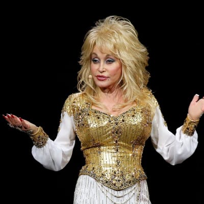 Dolly Parton står med armarna litet usträckta åt sidorna och händerna uppåt.