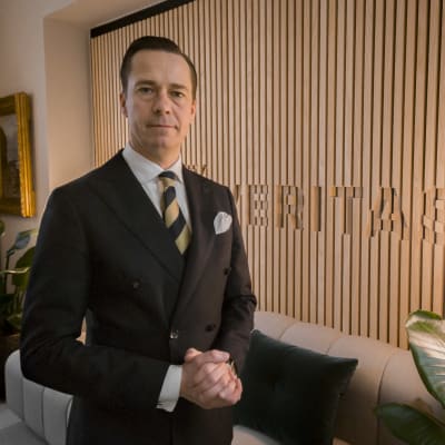 Carl Haglund står i Veritas kontor i Helsingfors iklädd mörk dubbelknäppt kavaj och slips . 