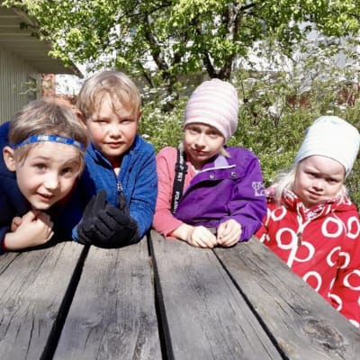 Fyra barn i dagisåldern vid ett bord utomhus.