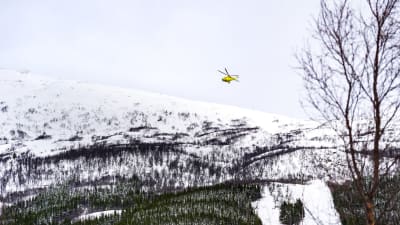 En helikopter flyger över snöklädda fjäll.