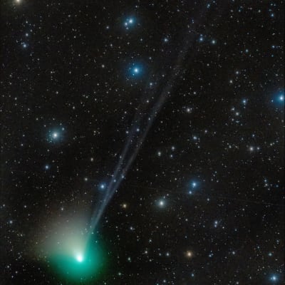 Rymden. Mörk bakggrund med en massa små stjärnor i olika färger, och en stor komet som ser ut som ett grönt klot åker förbi och lämnar en svag ljussvans efter sig.