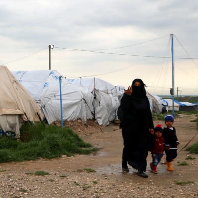 Mamma med barn framför läger i Syrien.
