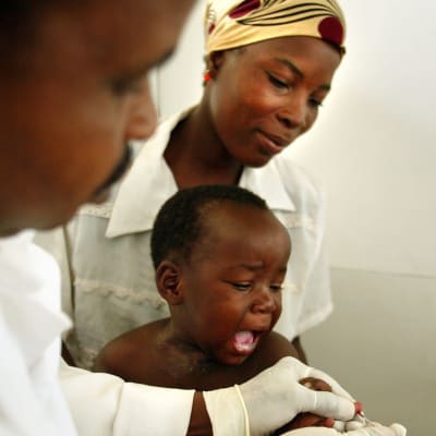 Ett barn i Afrika får vaccin. En kvinna håller i honom medan sjukskötaren sticker sprutan i barnet.