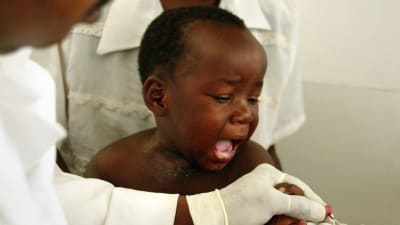 Ett barn i Afrika får vaccin. En kvinna håller i honom medan sjukskötaren sticker sprutan i barnet.
