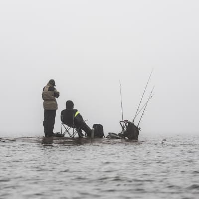 Kaksi miestä kalastaa sumun keskellä.