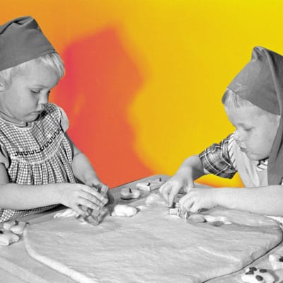 Kuvassa on kaksi lasta tonttulakit päässä leipomassa vuonna 1958