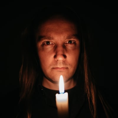 Kirjailija Mike Pohjola tuijottaa kameraan kynttilä kädessään pimeässä huoneessa.