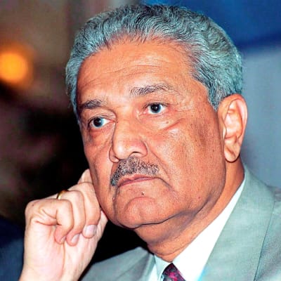 Abdul Qadeer Khan on kuvassa vaaleanharmaassa puvuntakissa ja punaisessa kravatisa. Hänellä on viikser ja harmaantuneet hiukset.