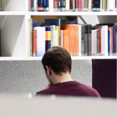 En studerande i Helsingfors universitets huvudbibliotek sitter med hörlurar i öronen och med ryggen vänd mot kameran.