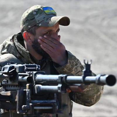 En soldat med Ukrainakeps håller handen för munnen. I förgrunden ett maskingevär.